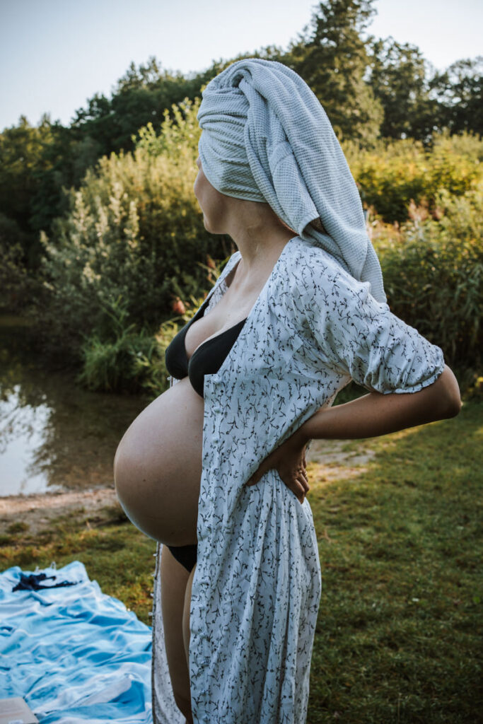 Schwangere-Frau-in-Bikini-offenem-Morgenmantel-mit-Handtuchturban-am-See