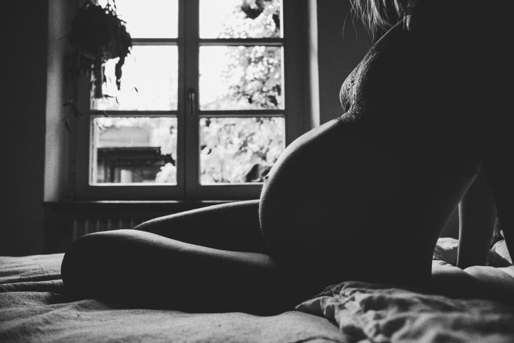 Schwarzweiß-Silhouette-von-schwangerem-Koerper-in-Unterwaesche-auf-Bett