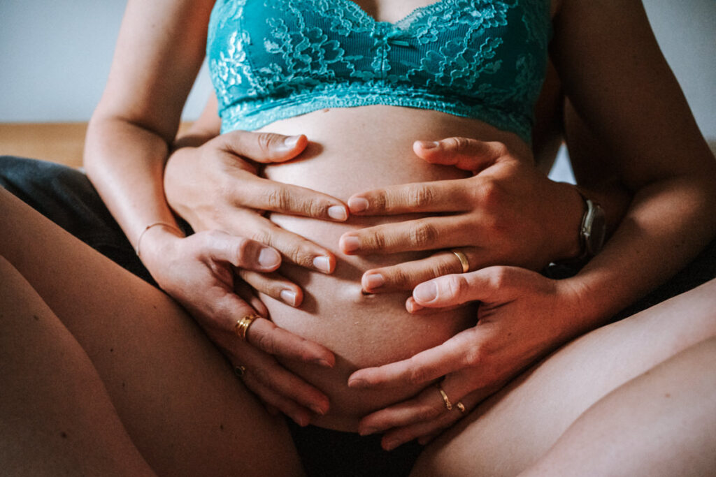 Haende-von-Paar-auf-schwangerem-Bauch-im-Schneidersitz-hintereinander