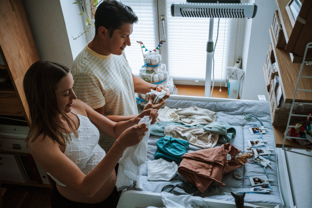 Schwangeres-Paar-faltet-Babykleidung-am-Wickeltisch-aus-Vogelperspektive