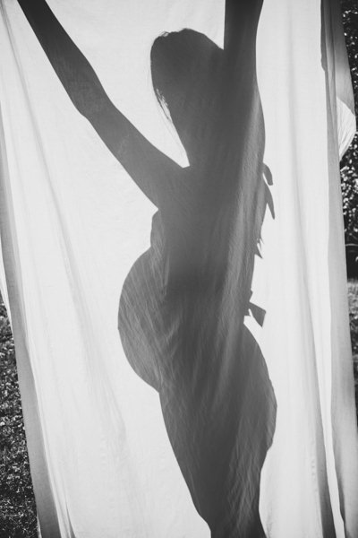 Schatten einer Schwangeren mit Babybauch hinter einem weißen Tuch