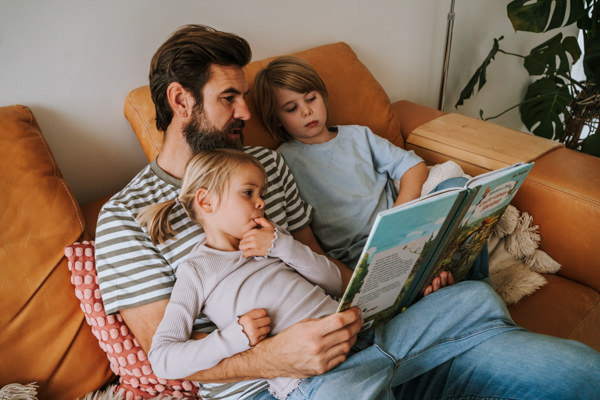Papa liest kuschelnden Kindern auf Sofa vor