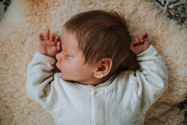Schlafendes Baby in weißem Langarm-Body auf flauschigem Teppich in Vogelperspektive