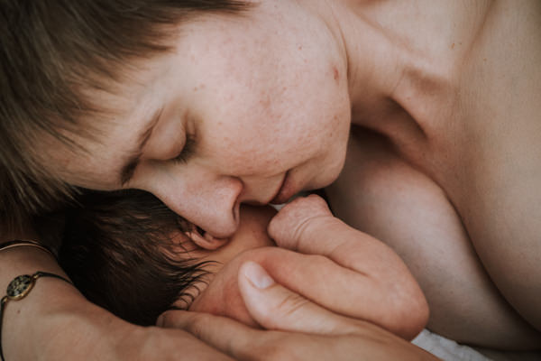 Nahaufnahme. Mama und Neugeborenes kuscheln Haut an Haut. Man sieht die Köpfe, Schultern und Hände.