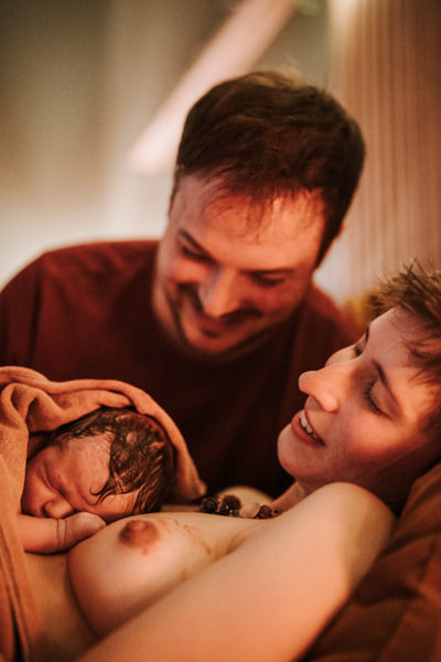 Eltern kuscheln mit noch blutverschmiertem Neugeborenen