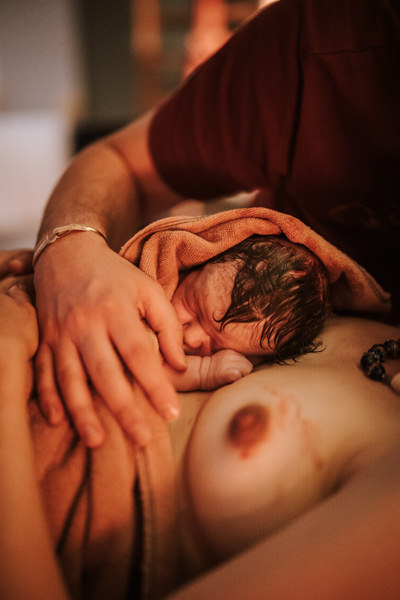 Neugeborenes im Handtuch liegt auf der Brust der Mama und wird von der Hand des Papas bedeckt